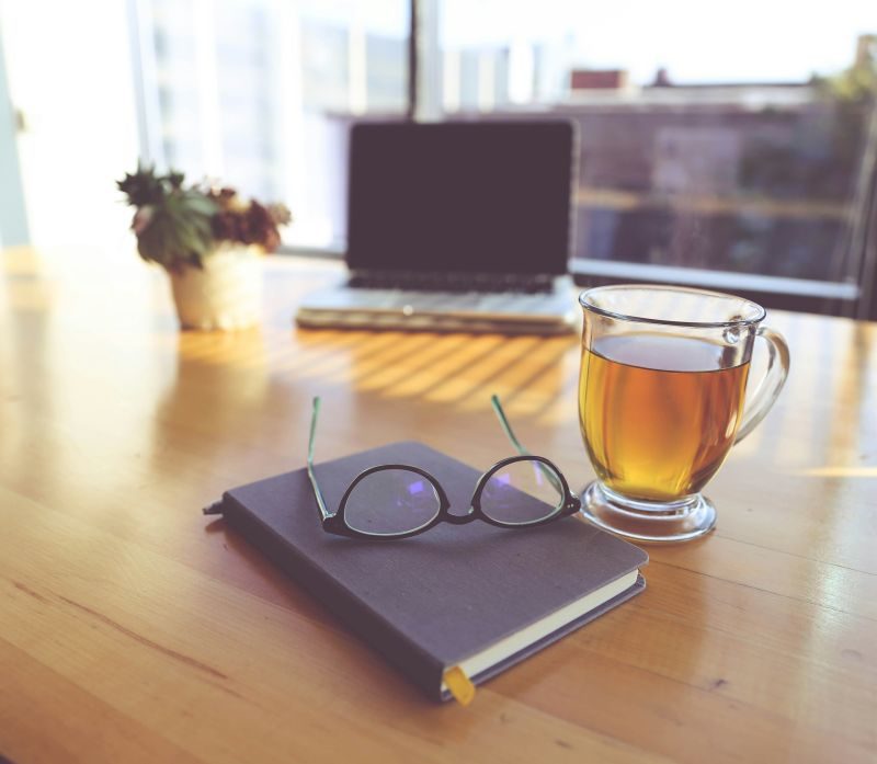 A cup of tea, glasses and a notebook on a wooden table