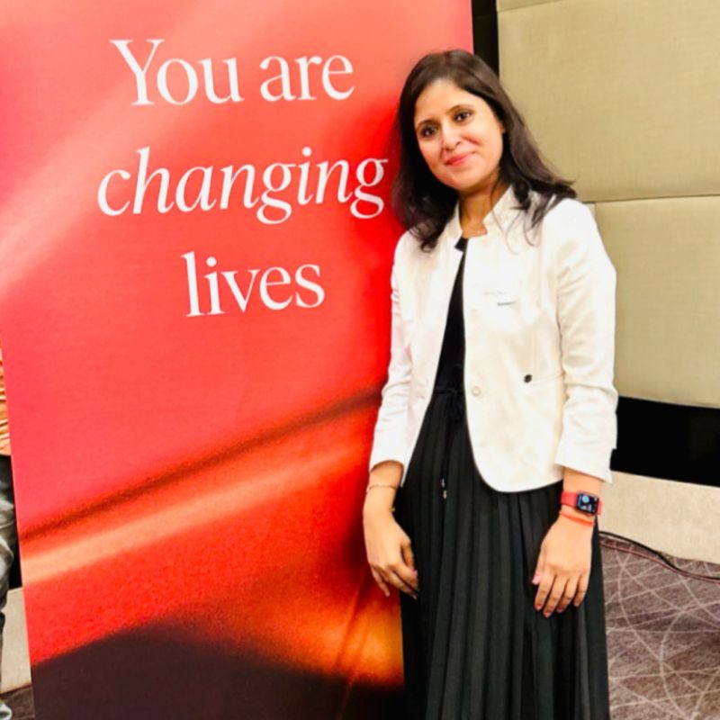 Gunjan Sinha standing beside a sign reading You are changing lives